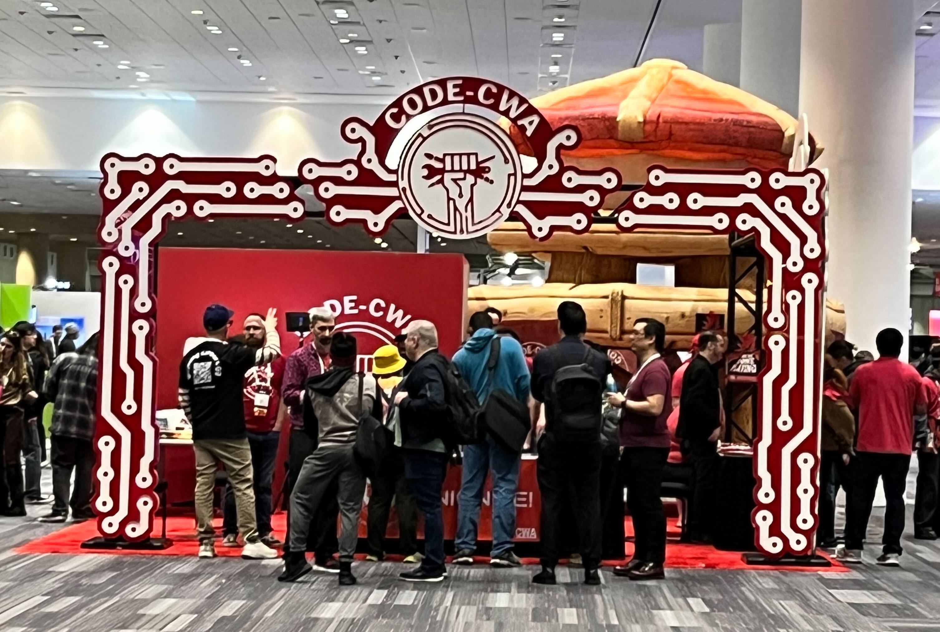The CWA booth at GDC 2025 The CWA booth at GDC 2025, decorated with red and white circuits. People are standing at the entrance to the booth, and above their heads is the CODE-CWA logo.